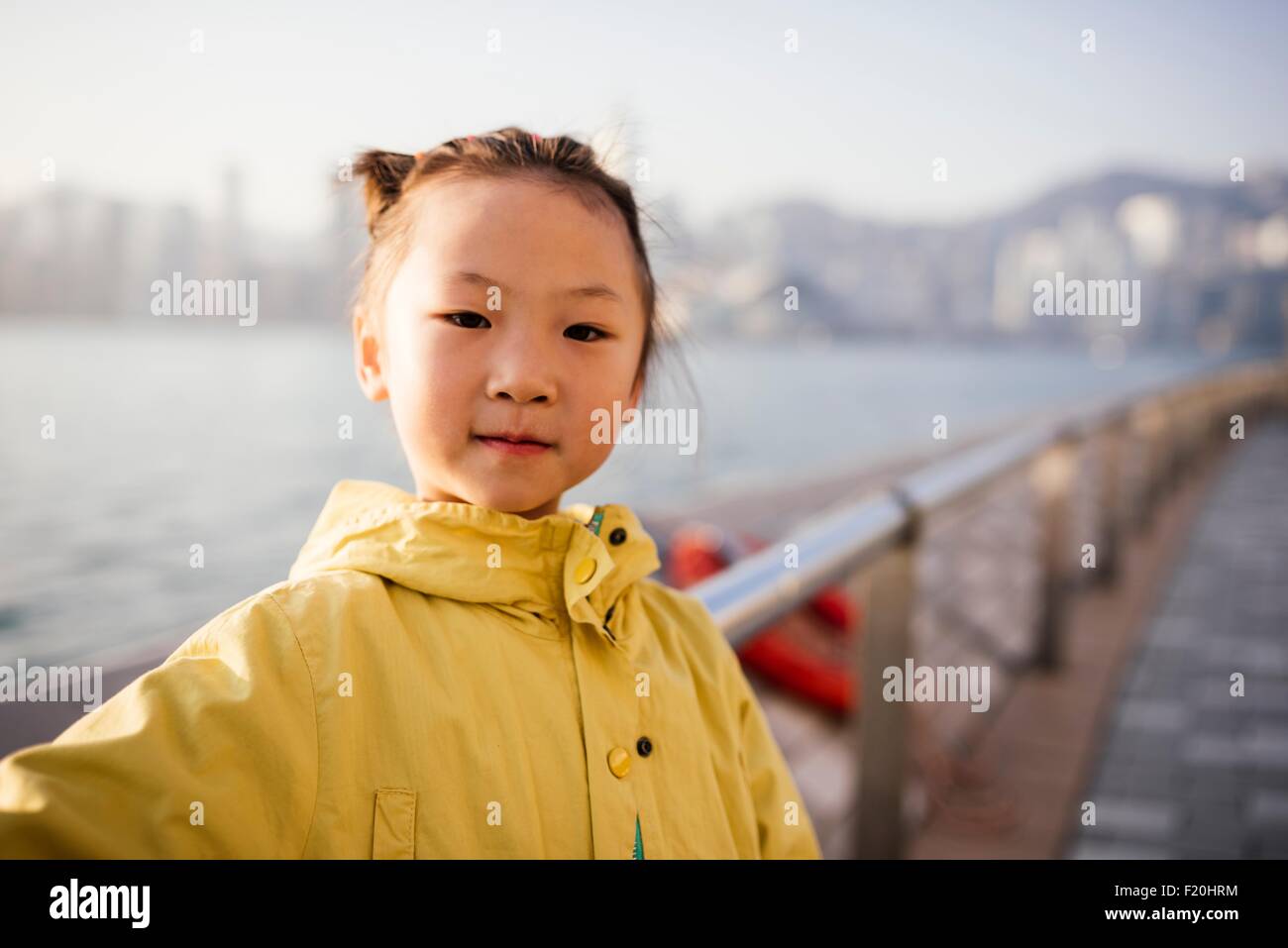 Portrait de jeune fille portant manteau jaune en face de l'eau looking at camera Banque D'Images