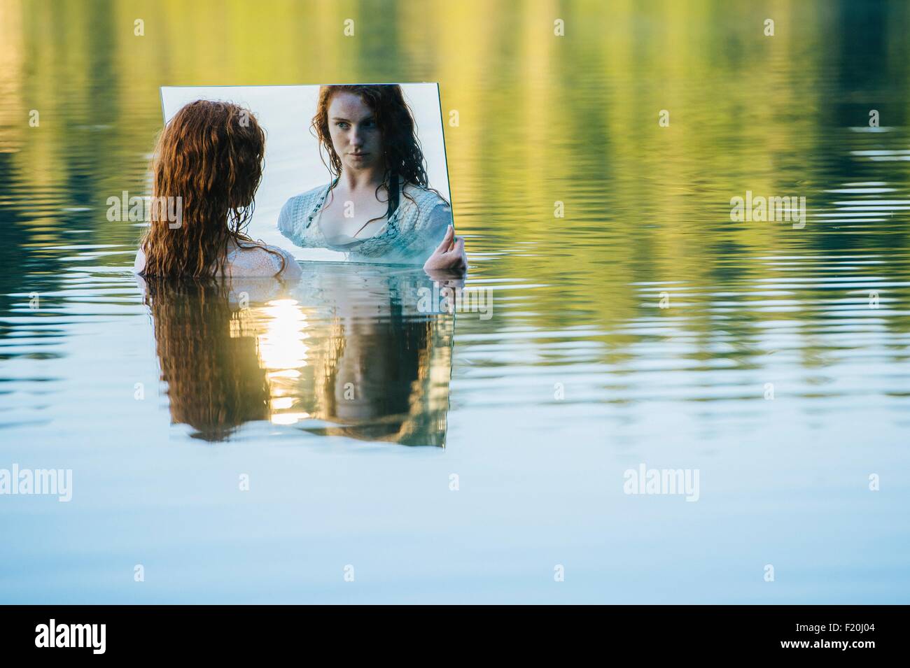 Jeune femme debout dans le lac, tenant un miroir, à la réflexion à Banque D'Images