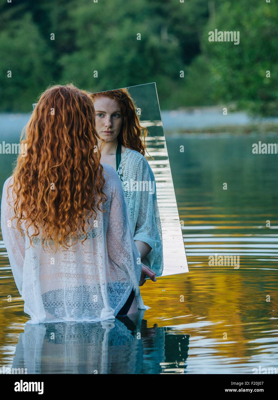 Jeune femme debout dans le lac, tenant un miroir, à la réflexion à Banque D'Images