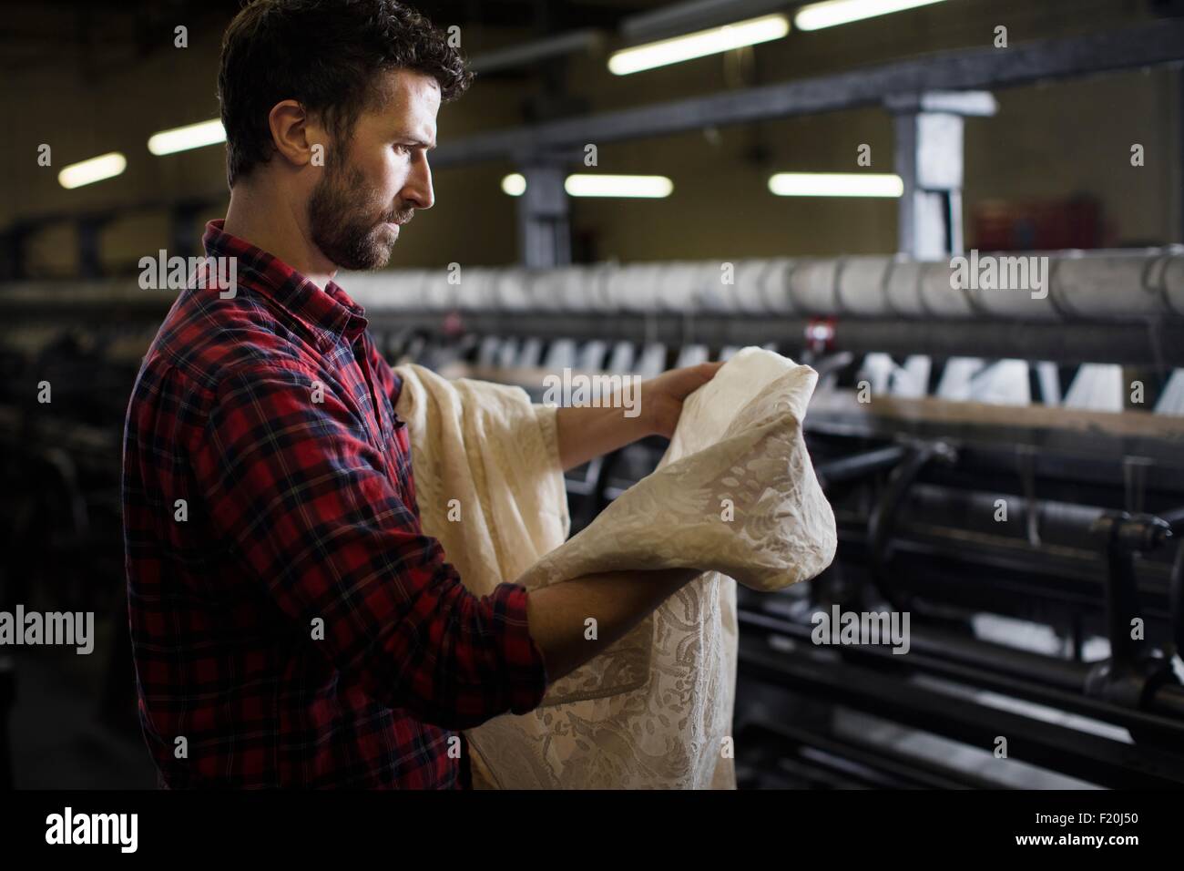 Portrait of male weaver examinant dentelle de vieille machine à tisser dans l'usine de textile Banque D'Images
