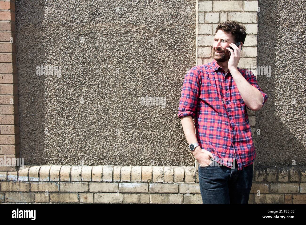 Young man leaning against wall chatting on smartphone Banque D'Images