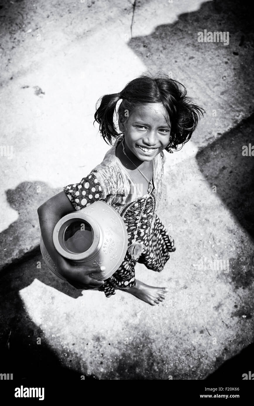 Indian girl portant un pot en plastique avec de l'eau d'un tube de mesure dans un village de l'Inde rurale . L'Andhra Pradesh, Inde. Noir et blanc. Banque D'Images