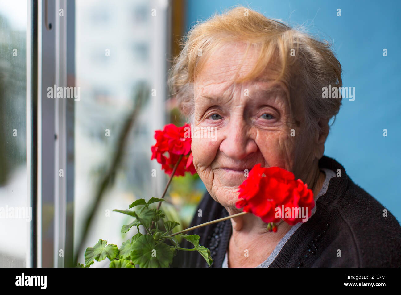 Portrait d'une vieille femme sur le balcon avec des fleurs rouges. Banque D'Images