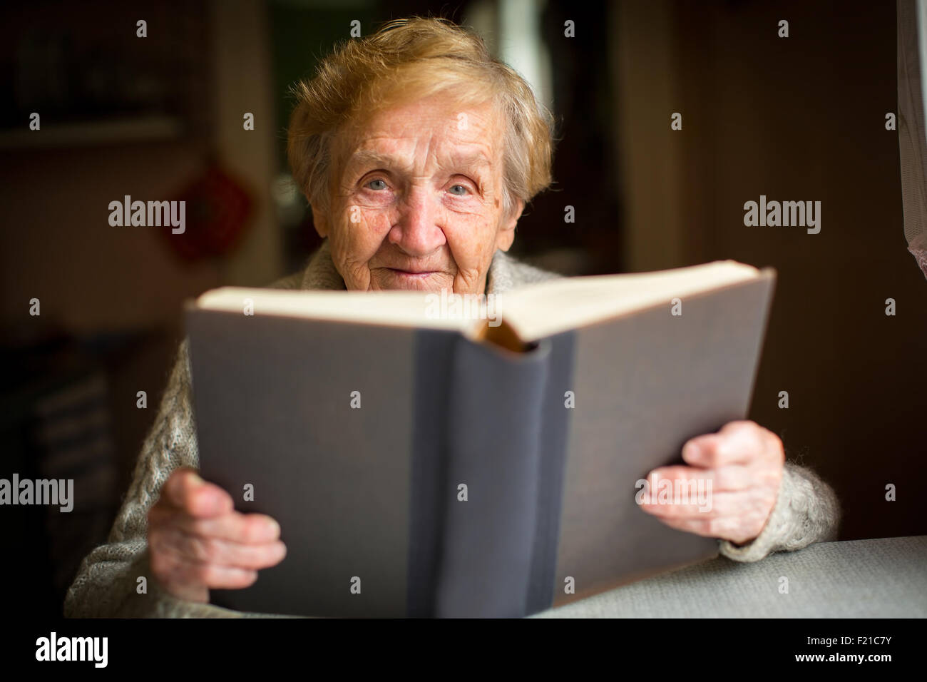 Une femme âgée de la lecture d'un gros livre assis à une table dans la chambre. Banque D'Images