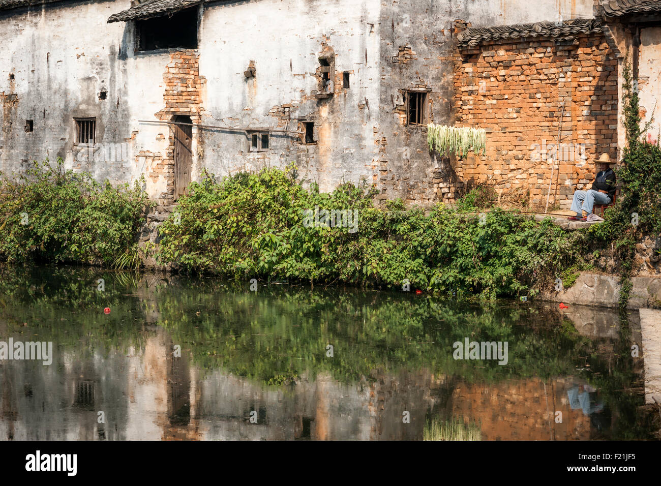 Homme est assis à l'ombre près de haricots sèchent sur un patio donnant sur l'eau, village de Chengkan, China, Asia Banque D'Images