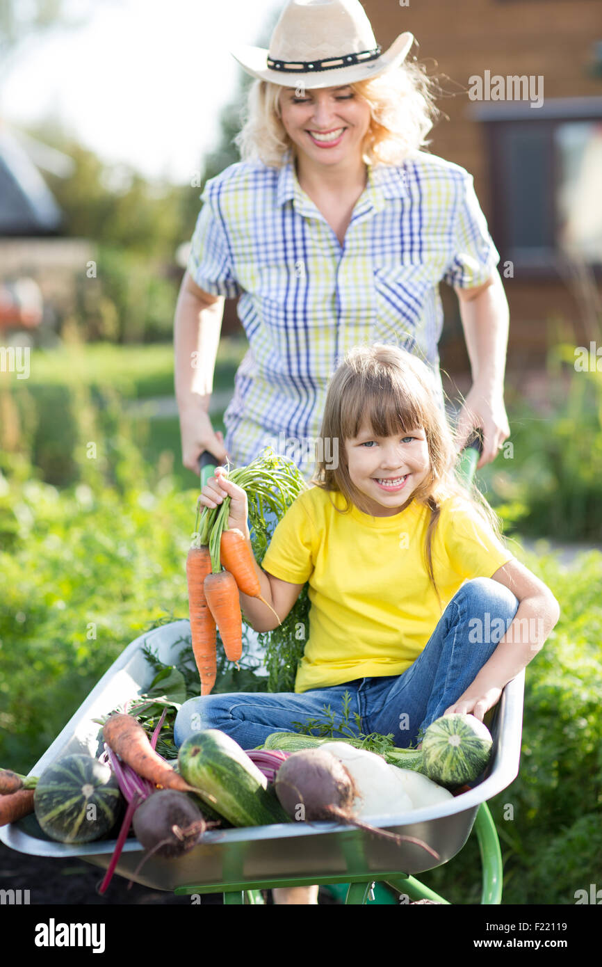 Mère et enfant dans un jardin intérieur. Enfant assis dans la brouette avec des légumes de la récolte. Les légumes biologiques sains pour les enfants. Banque D'Images