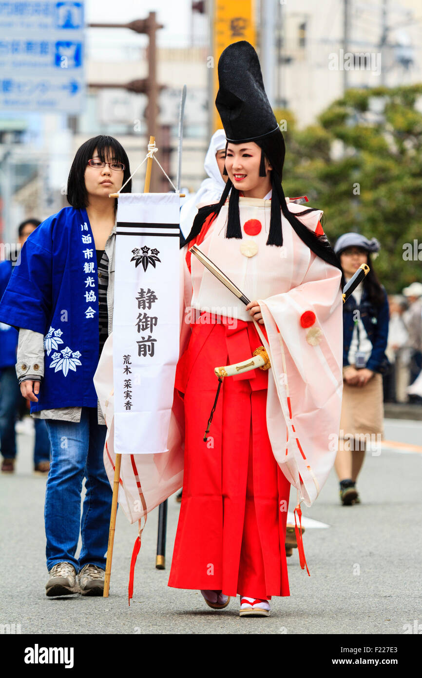 Défilé du festival de Genji, Japon. Tada Jeune femme habillée en danseuse shirabyoshi Heian, avec une longue jupe rouge, chemisier blanc, et grand chapeau noir. En souriant. Banque D'Images