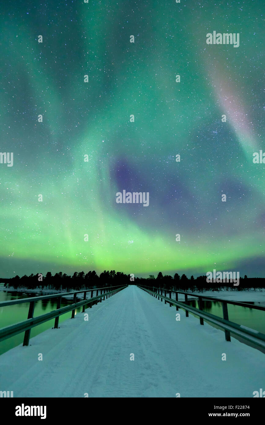 Des aurores boréales) sur un pont et une rivière dans un paysage d'hiver enneigé en Laponie finlandaise. Banque D'Images