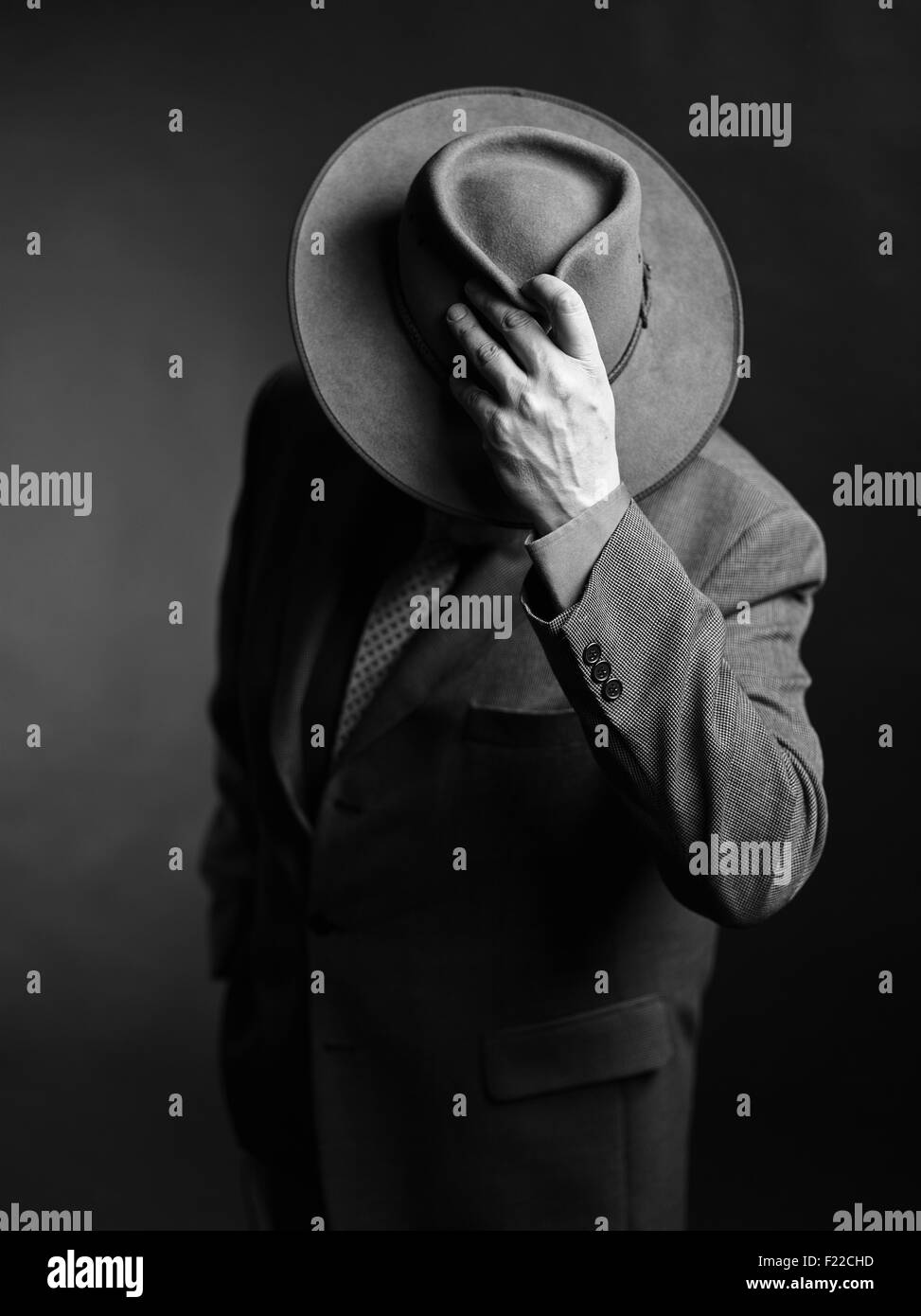 Homme portant costume sombre et il couvrant le visage avec un chapeau, noir et blanc Banque D'Images