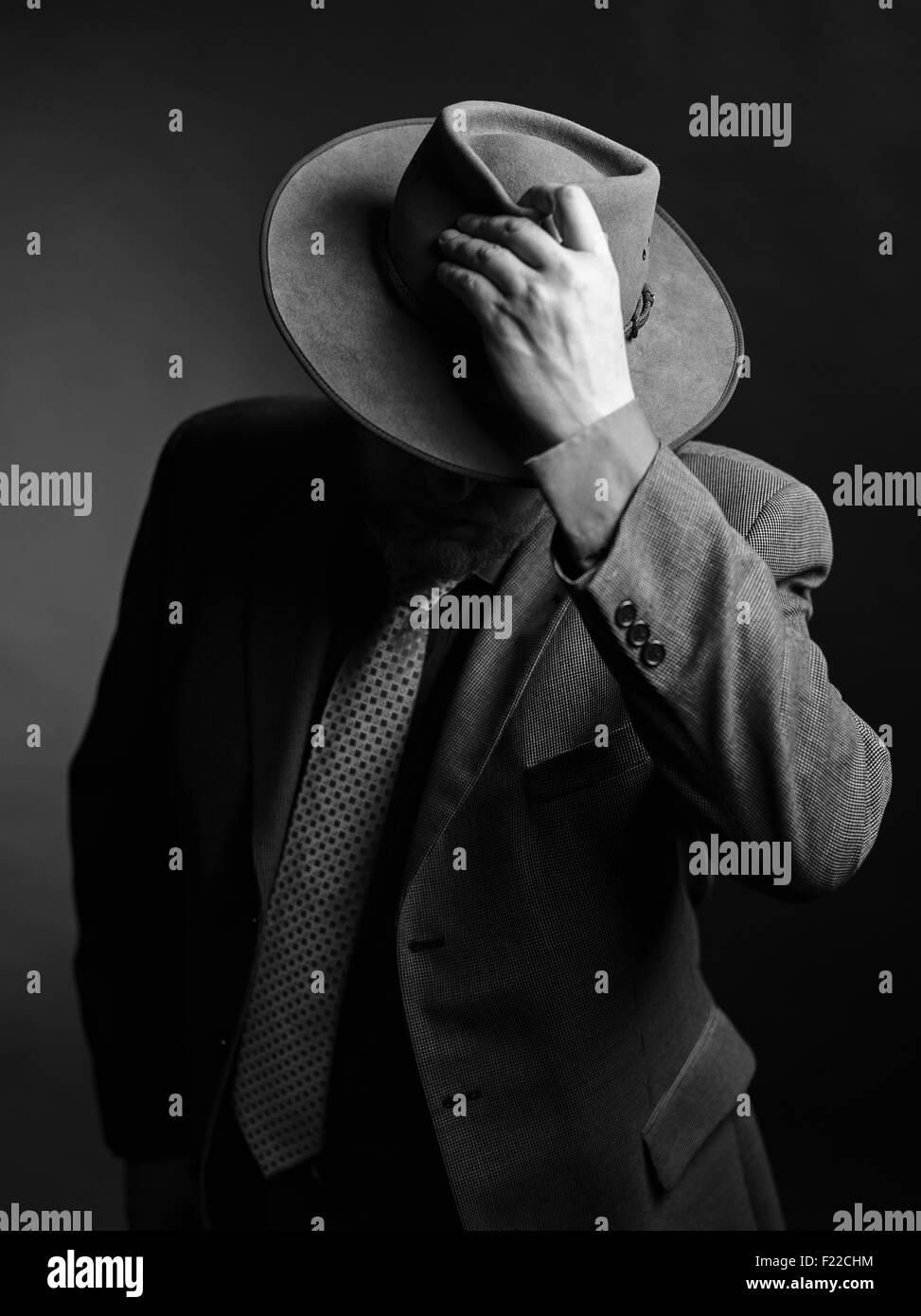 Homme portant costume sombre et il couvrant le visage avec un chapeau, noir et blanc Banque D'Images