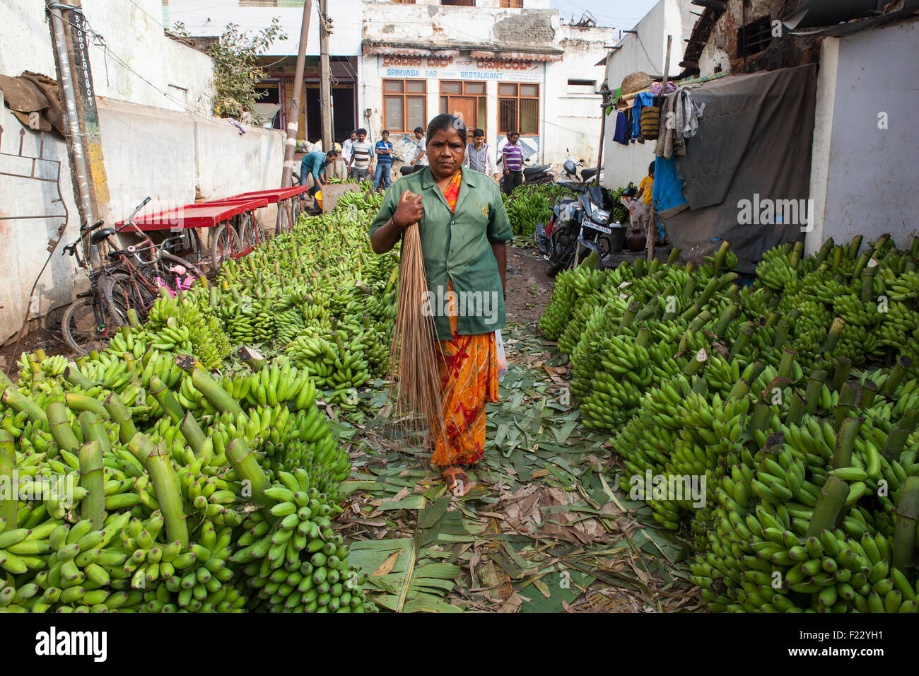 Une femme de ménage tenant un balai de promenades à travers les rayonnages et rangées de bananes à l'Devaraja market à Mysore Banque D'Images
