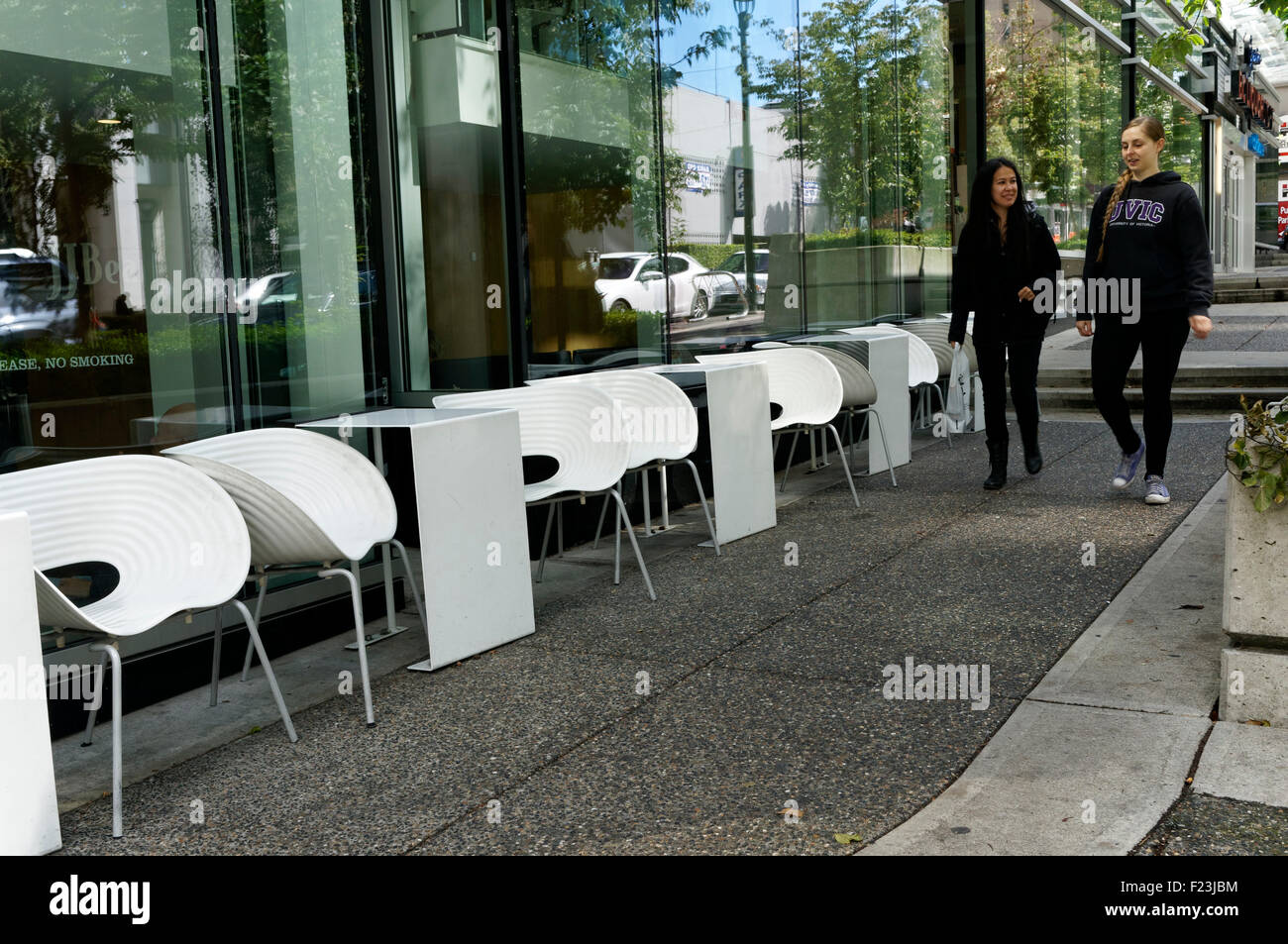 Deux jeunes femmes marchant par outdoor cafe tables blanc au centre-ville de Vancouver, BC, Canada Banque D'Images