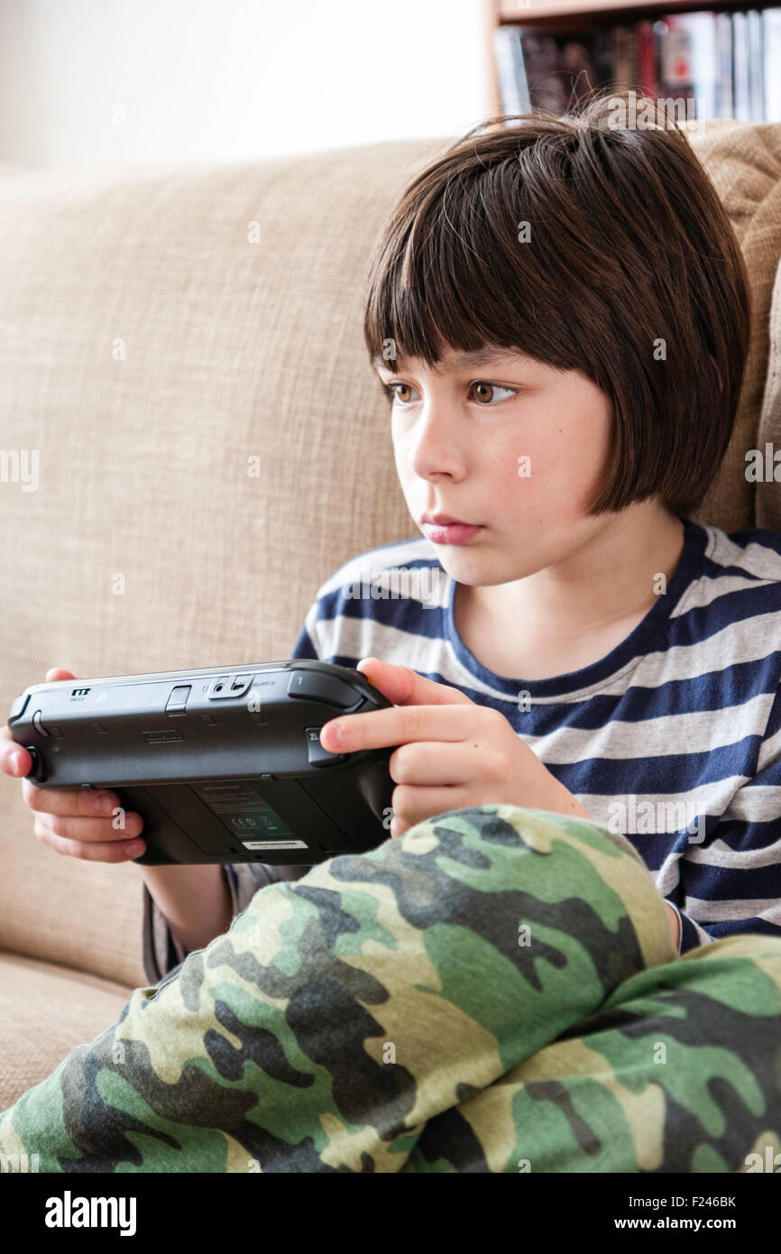 Homme caucasien enfant, garçon, 10-12 ans, assis tenant une console de jeu Nintendo Wii en concentrant les deux mains, la tête et épaules Vue de côté. Banque D'Images