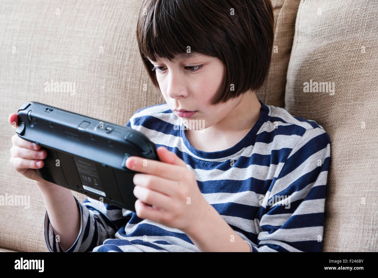 Homme caucasien enfant, garçon, 10-12 ans, assis tenant une console de jeu Nintendo Wii en concentrant les deux mains, la tête et épaules Vue de côté. Banque D'Images