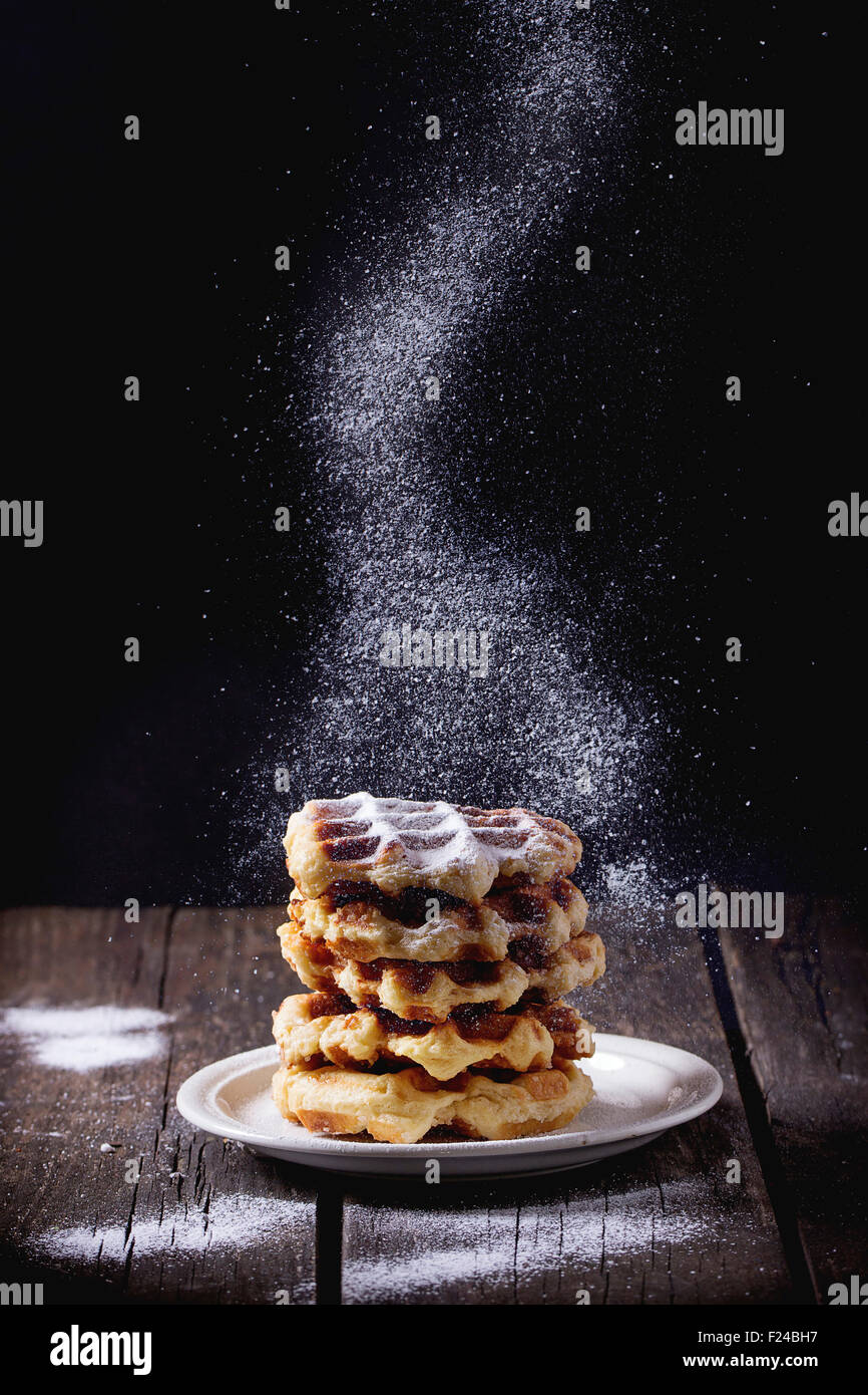 Plaque blanche avec des gaufres belges faites maison avec du sucre en poudre Tamiser sur fond noir. sucre glace plus vieille table en bois. D Banque D'Images