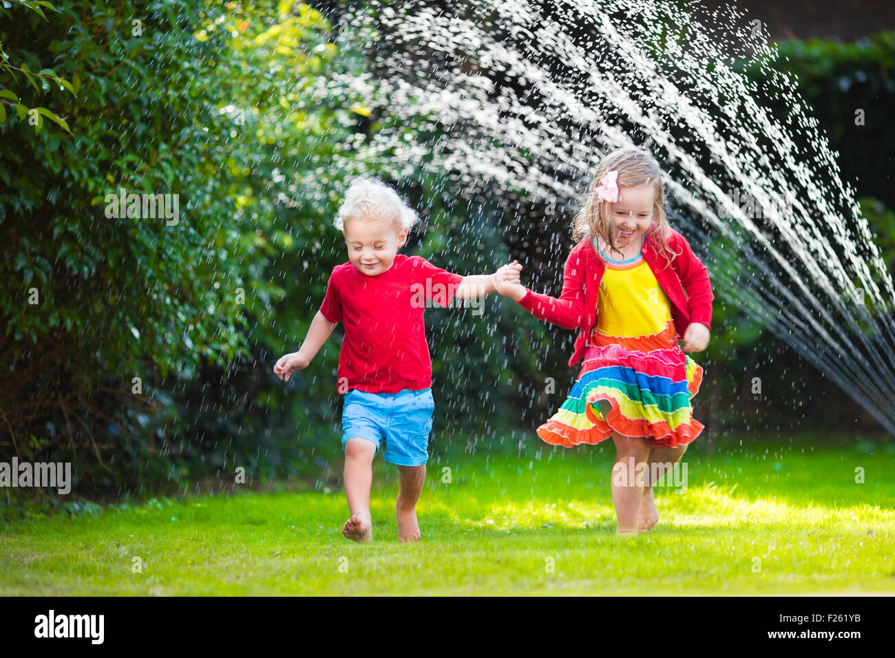 Enfant jouant avec jardin arroseur. Enfant d'âge préscolaire la course et le saut. Piscine d'été de plaisir de l'eau dans la cour. Banque D'Images
