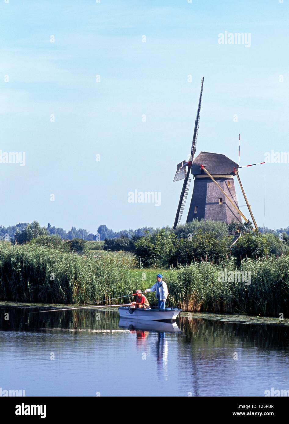 Deux hommes de l'endroit de la pêche sur la digue d'un moulin à vent à l'arrière, Kinderdijk, Hollande, Pays-Bas, l'Europe. Banque D'Images