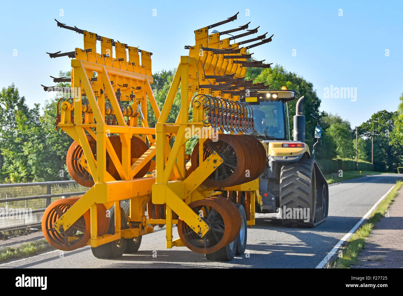 Agriculteur qui conduit un tracteur Challenger Caterpillar de grande taille remorquant un équipement agricole de herse à disque plié dans une ruelle de campagne étroite Essex Angleterre Royaume-Uni Banque D'Images