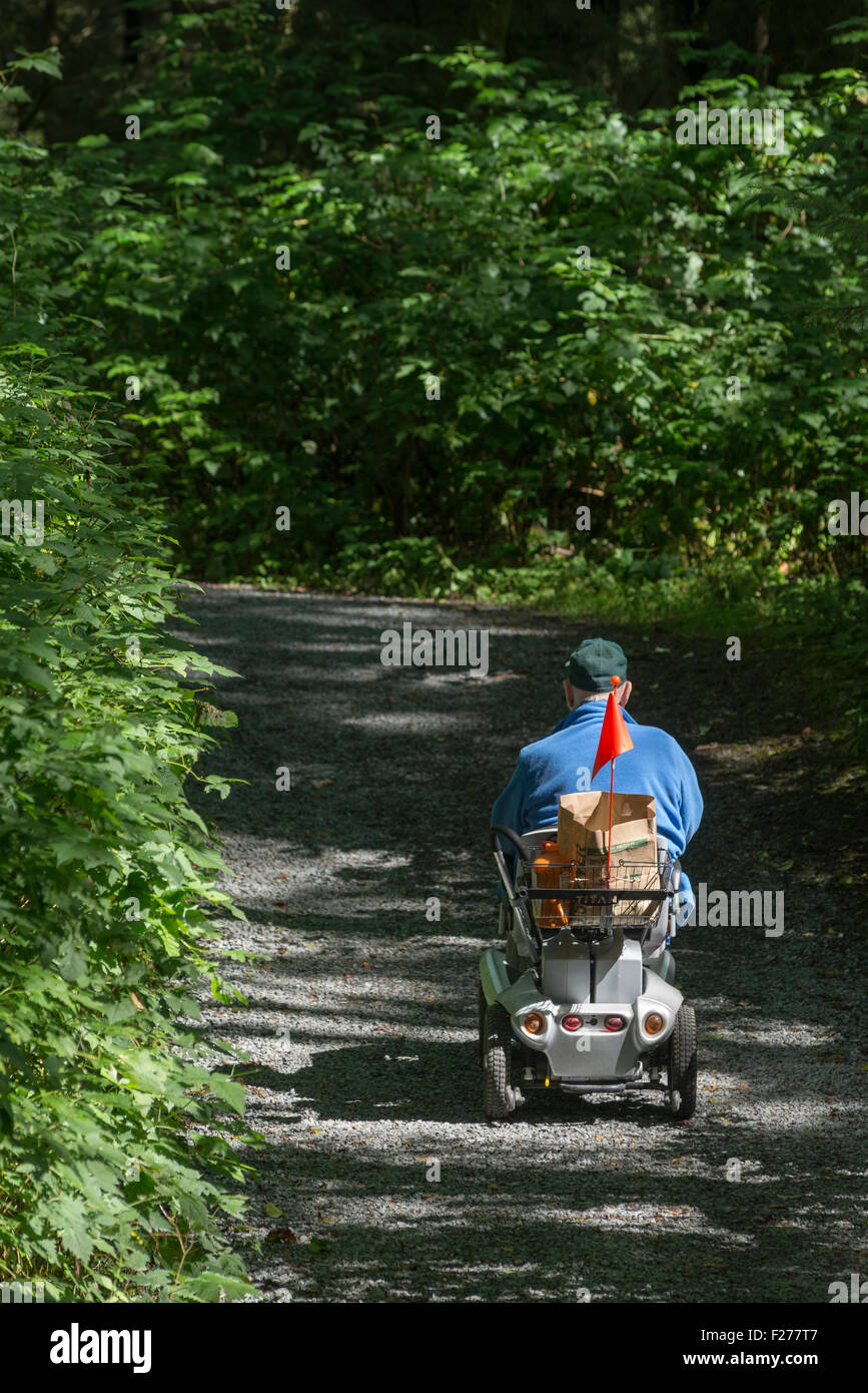 L'homme en fauteuil roulant motorisé sur un sentier dans le parc historique national de Sitka, Sitka, Alaska. Banque D'Images
