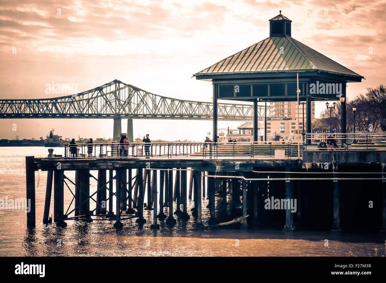 Personnes pour le coucher du soleil sur la jetée surplombant le majestueux fleuve du Mississippi avec le Crescent City Connection Bridge à distance, New Orleans, LA, Banque D'Images