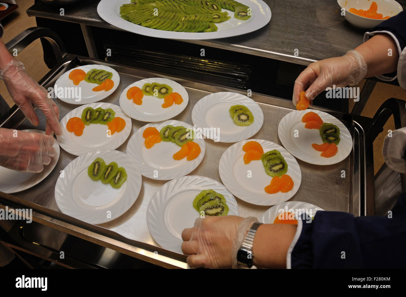 Un traiteur prépare des plats de dessert avec des tranches de kiwi et orange. Banque D'Images