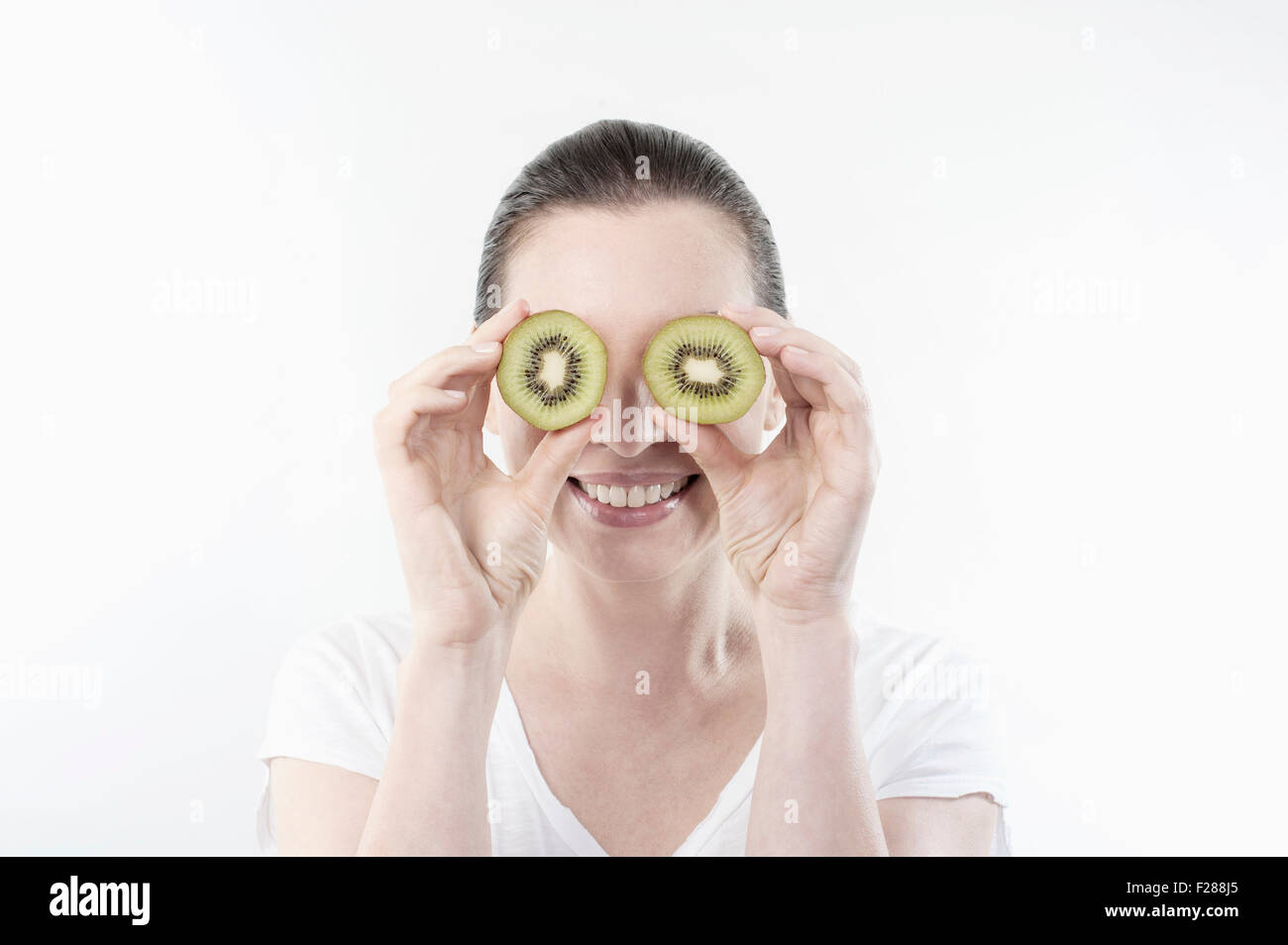 Mature Woman holding tranches de kiwi devant ses yeux, Bavière, Allemagne Banque D'Images