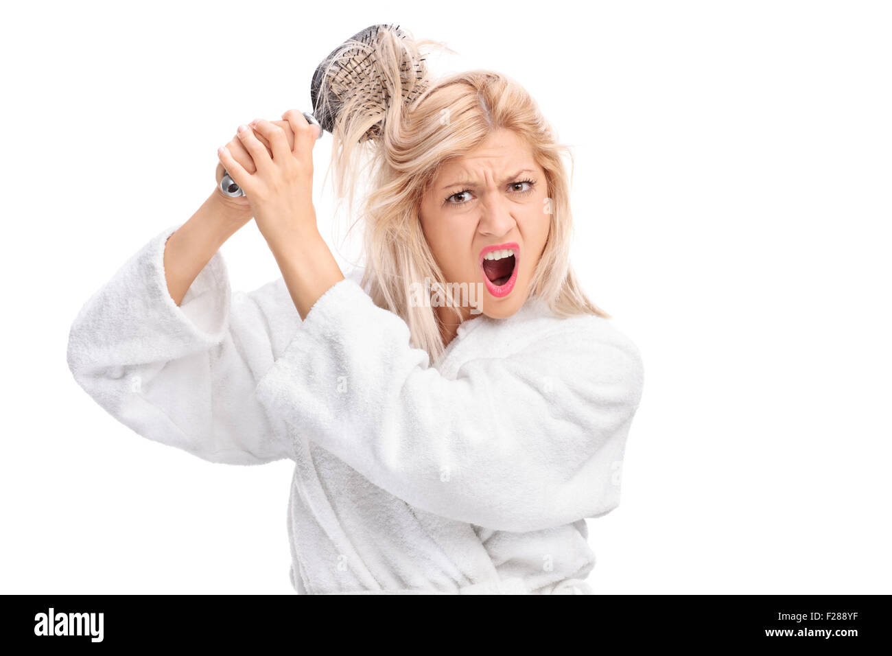 Fille mécontent dans un peignoir blanc avec ses cheveux emmêlé dans une brosse à cheveux isolé sur fond blanc Banque D'Images