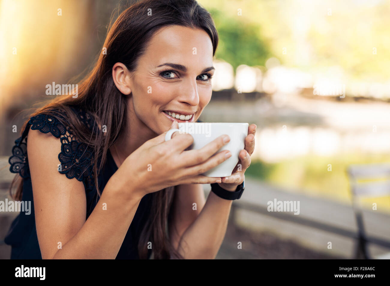 Belle Jeune femme tenant une tasse de café à la caméra en souriant. Femmes gaies savourer une tasse de café au café. Banque D'Images