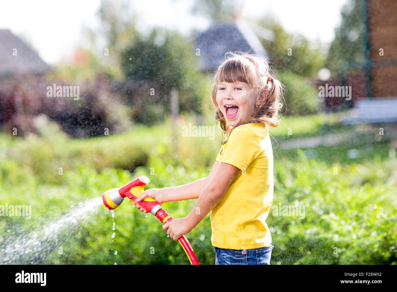 Happy girl verse de l'eau d'un tuyau flexible dans jardin Banque D'Images