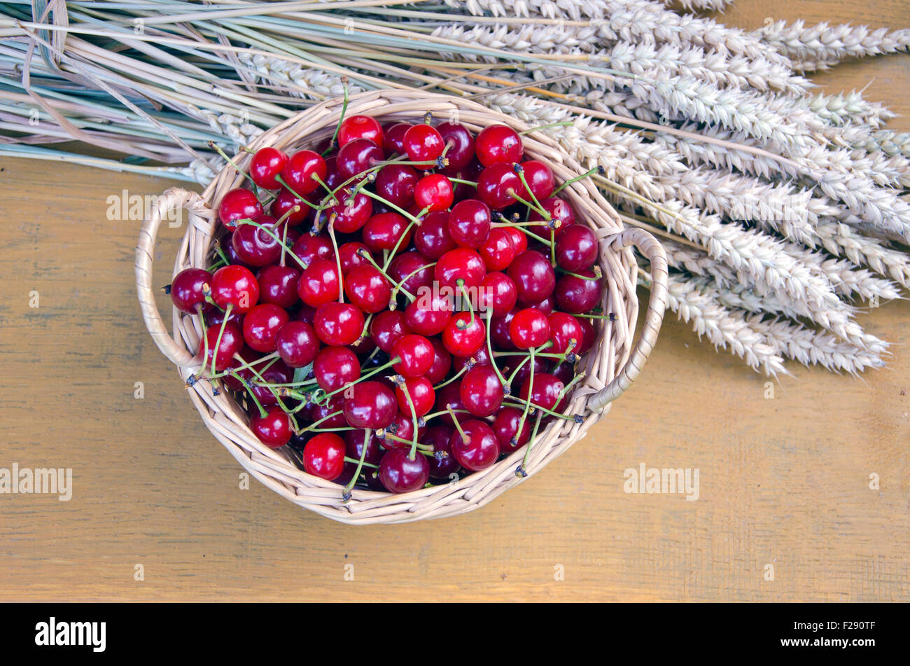 Cerises cueillies dans panier en osier avec du blé sur fond de bois Banque D'Images