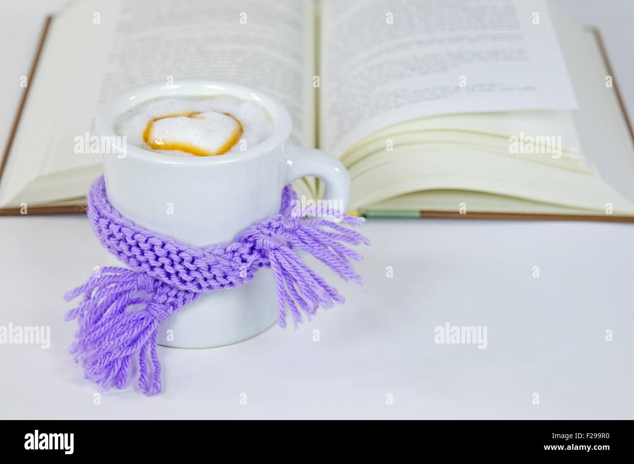 Tricot d'hiver mauve foulard enroulé autour d'un cappuccino boisson avec coeur et livre sur blanc. Banque D'Images
