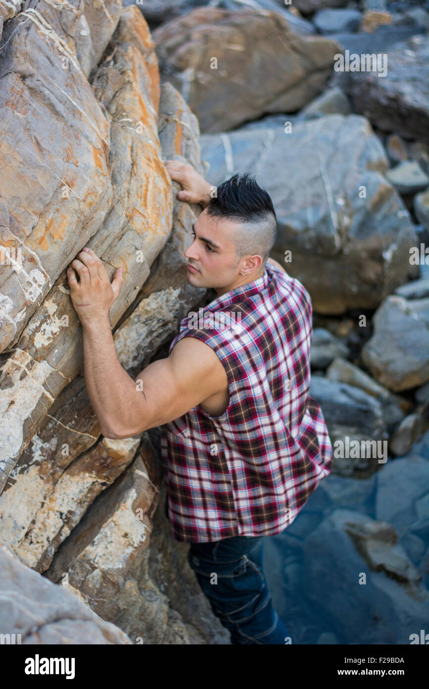 Trois quart d'un joli coup de jeune homme athlétique escalade un rocher à la rivière ou à la mer ou l'Océan Banque D'Images