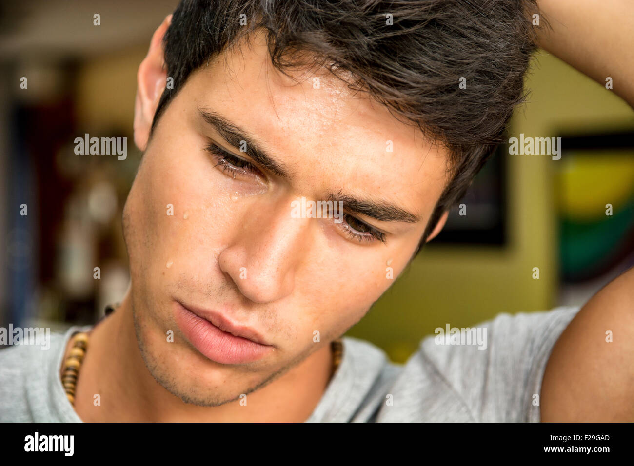 Close up visage d'un beau jeune homme pensif avec des larmes sur son visage, regardant vers le bas, inquiets ou tristes. Banque D'Images