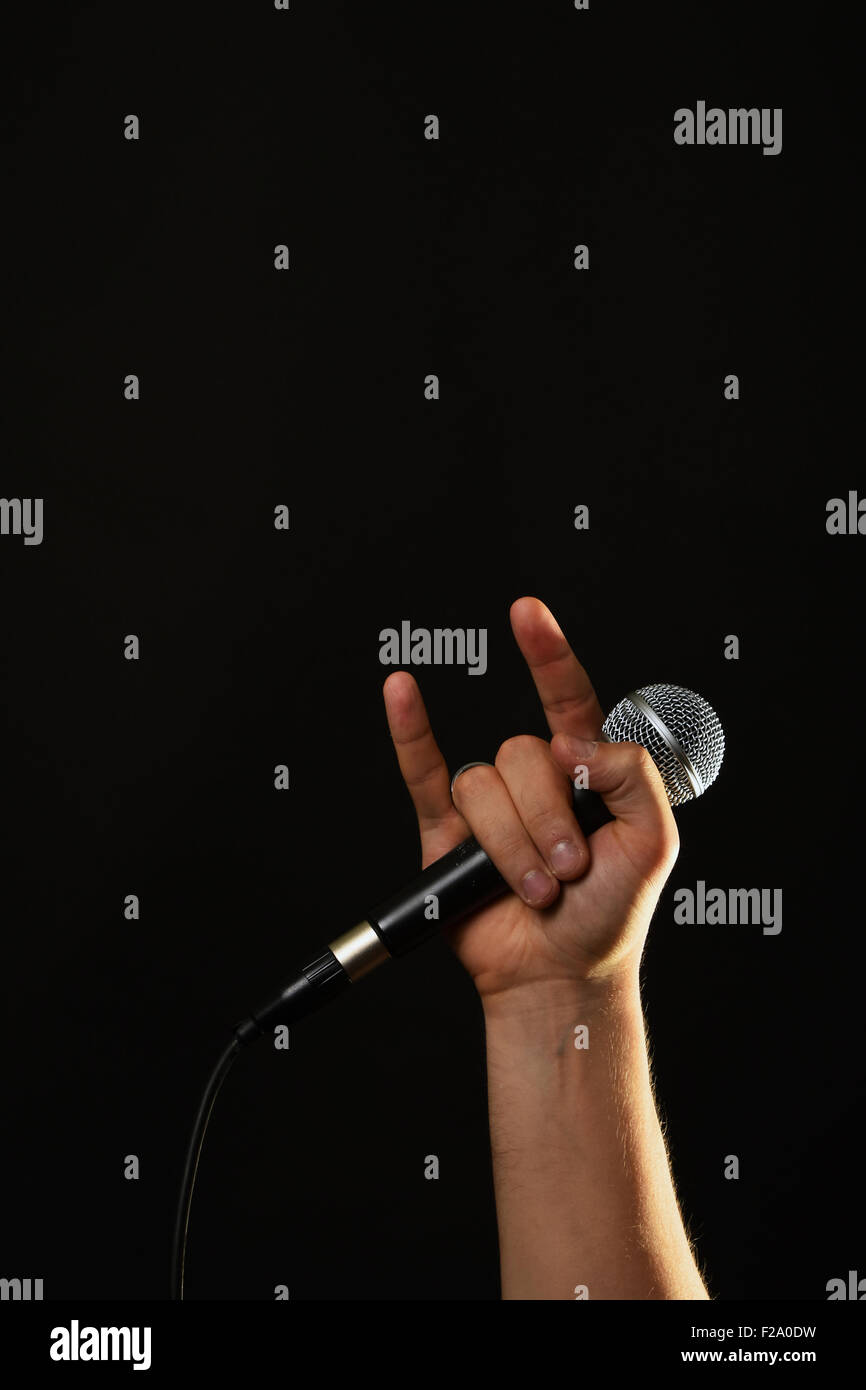 Homme hand holding microphone avec cornes de diable rock metal sign isolé sur fond noir Banque D'Images