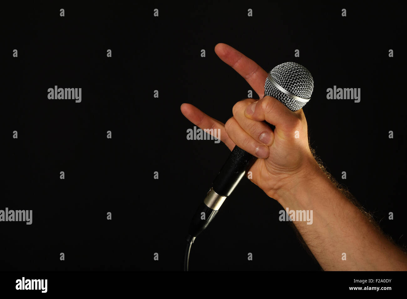 Homme hand holding microphone avec cornes de diable rock metal sign isolé sur fond noir Banque D'Images