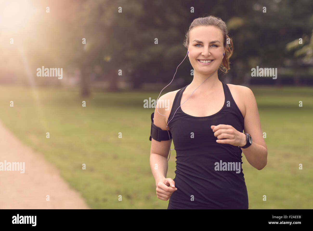 Moitié du corps, tourné d'une jolie femme athlétique jogging au parc avec des écouteurs et souriant à la caméra, avec copie espace Banque D'Images