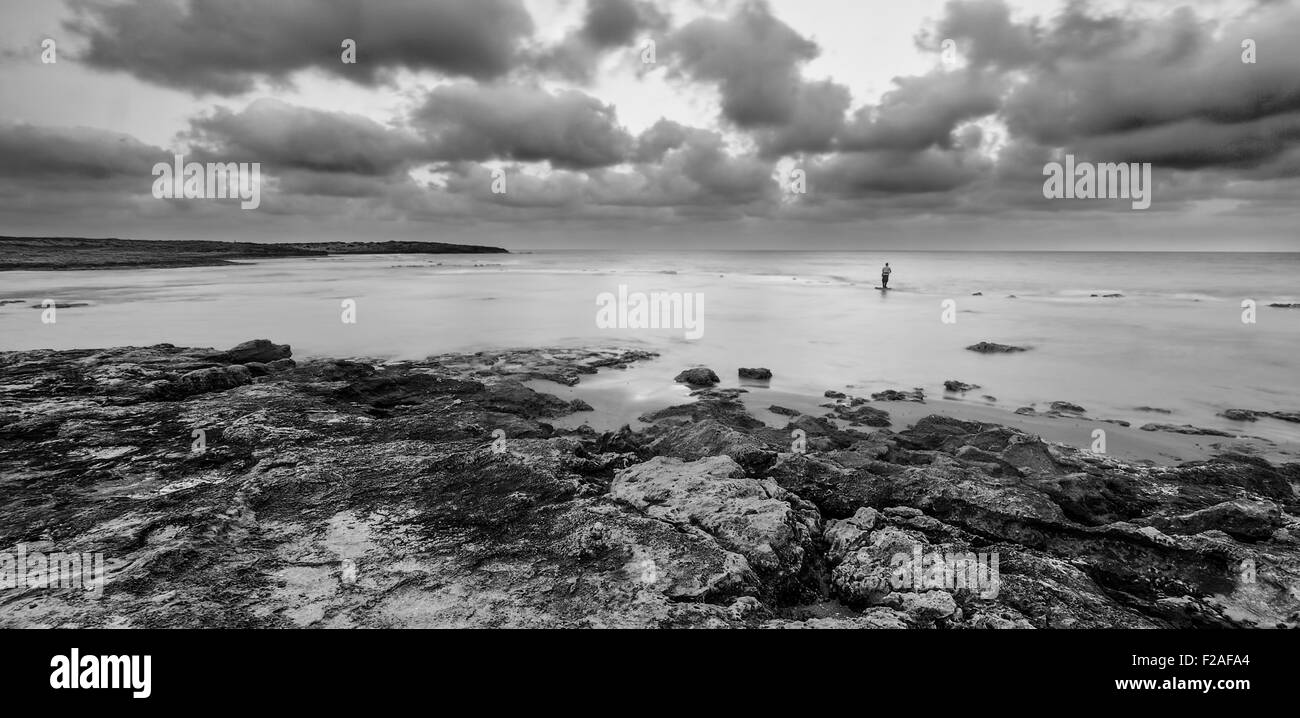 Pêcheur solitaire debout dans l'eau au lever du soleil, à la plage Dor, Israël en noir et blanc Banque D'Images