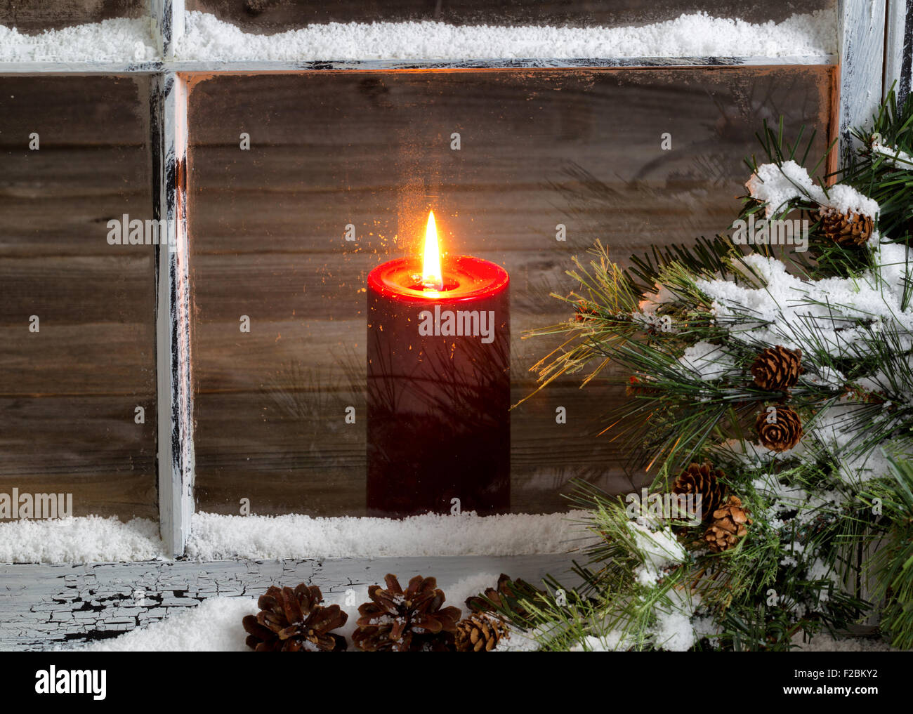 Fenêtre décorée avec glowing bougie rouge, selective focus on flame et partie supérieure de bougie, les cônes de pin, et la neige à l'extérieur. Banque D'Images