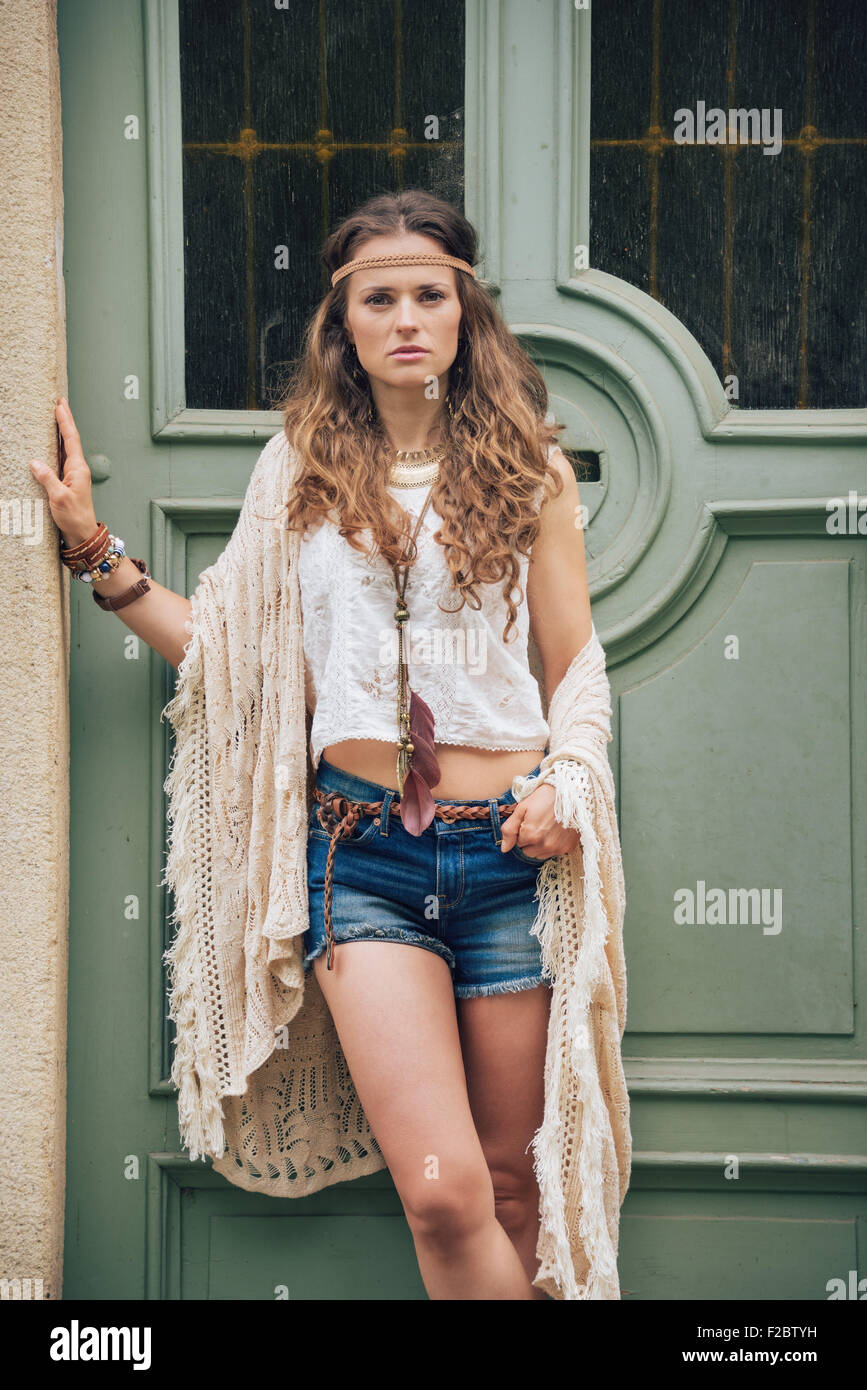 Portrait de femme brune-hippie à la recherche dans les jeans, shorts et  châle tricoté blouse blanche à l'extérieur debout contre la porte en bois  je Photo Stock - Alamy