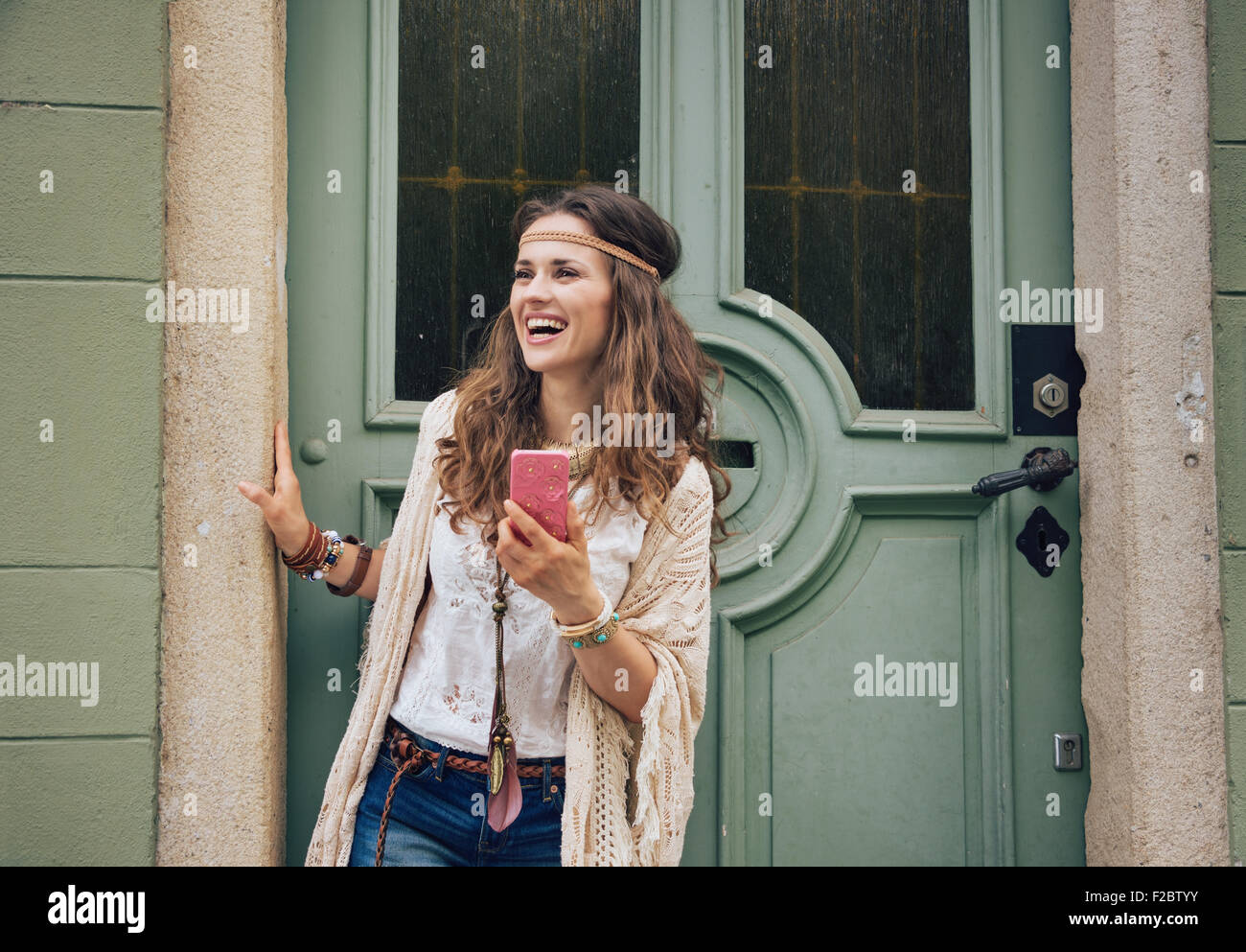 La mode femme hippie heureux avec un téléphone mobile en jeans short, chemisier blanc et châle tricoté en extérieur permanent contre woo olive Banque D'Images