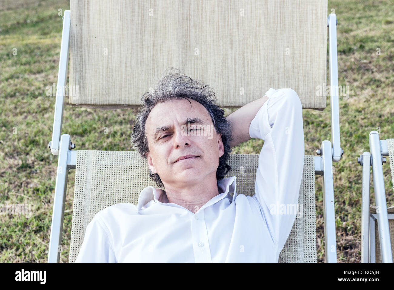 Retraite d'été loin du stress - charmante Caucasian homme d'âge moyen avec des cheveux gris et chemise blanche posée sur une chaise longue dans la campagne Banque D'Images