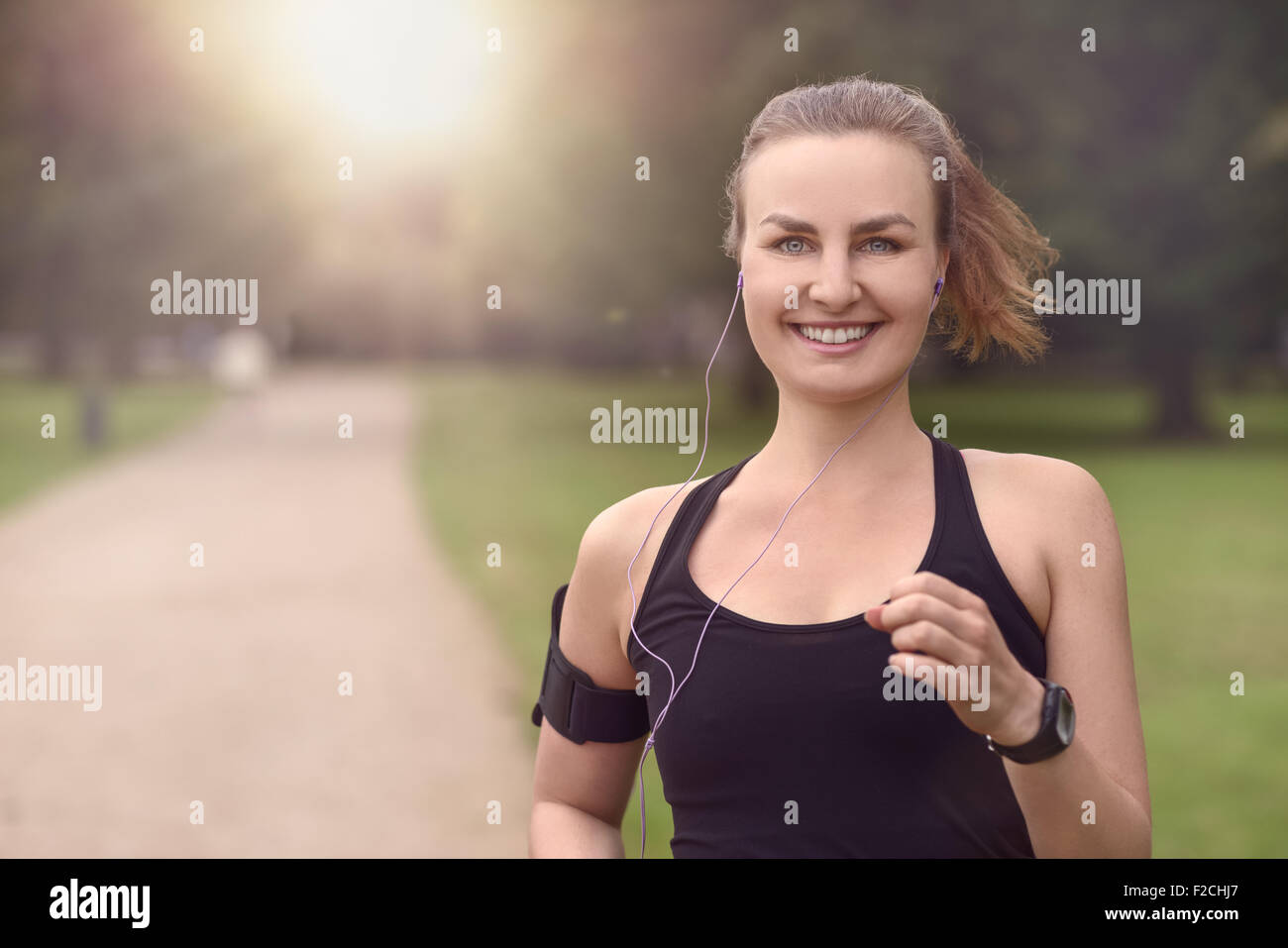 Moitié du corps, tourné d'une jolie femme athlétique jogging au parc avec des écouteurs et souriant à la caméra, avec copie espace Banque D'Images
