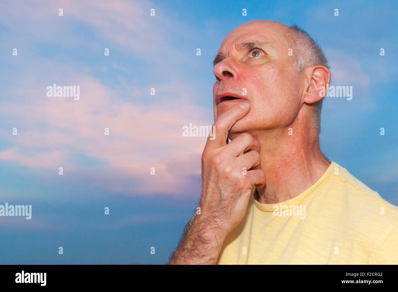 A senior man posing with thoughtful, sérieux et expressions idiotes à l'extérieur contre un ciel bleu. Banque D'Images