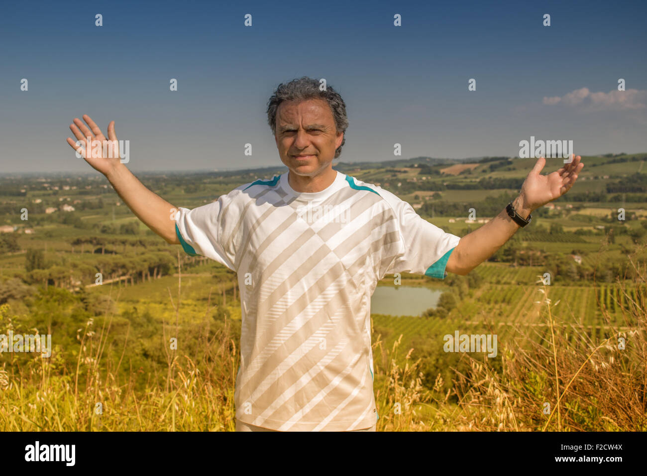 Beau jeune homme de 40 ans avec des cheveux poivre sel habillé avec sports shirt ouvre ses bras