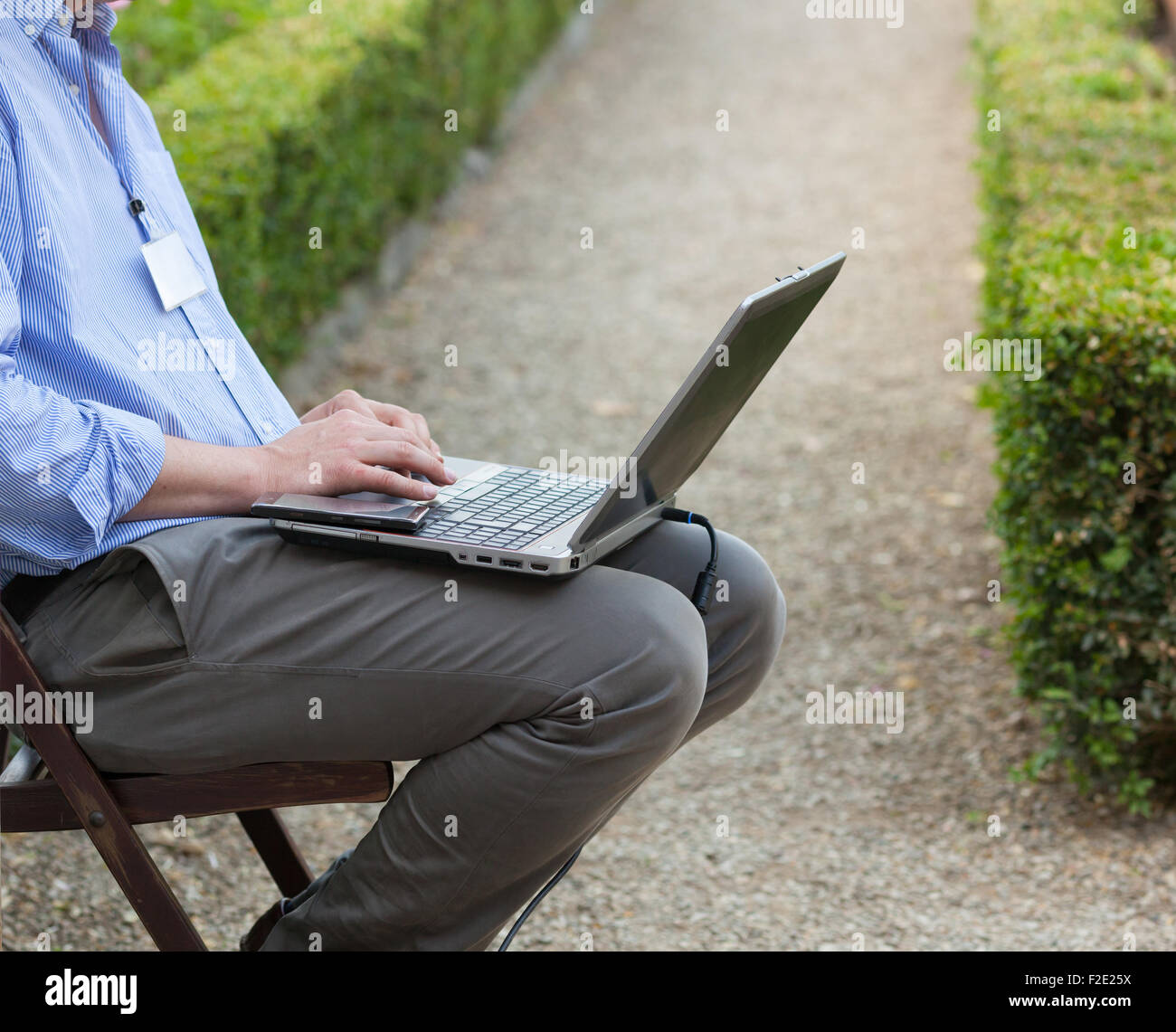 Portrait de l'ordinateur portable sur ses genoux et en regardant l'ordinateur portable tout en étant assis à l'extérieur. Banque D'Images