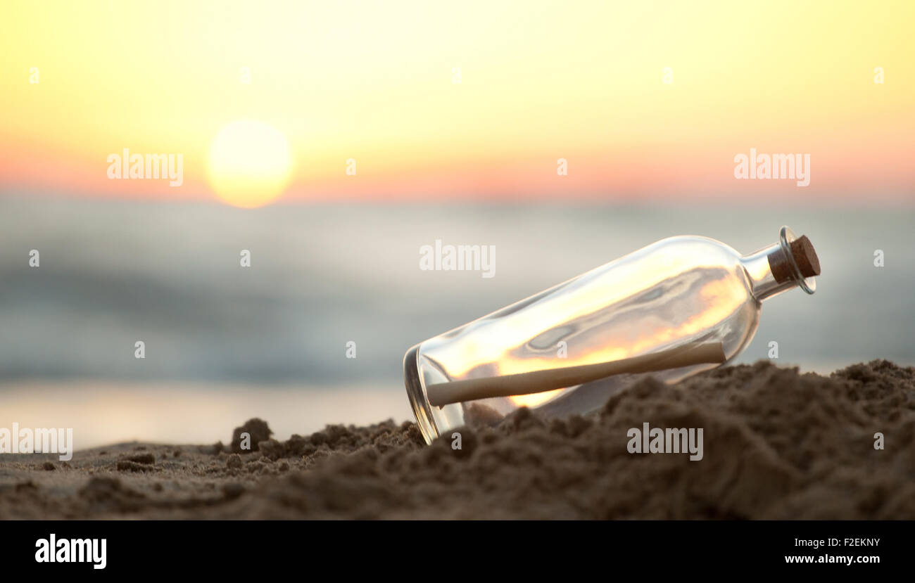 Message dans une bouteille en verre sur une plage avec lever du soleil en arrière-plan Banque D'Images