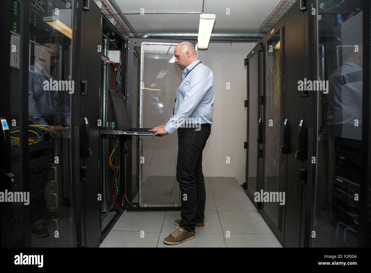 Spécialiste de l'informatique travaillant sur des serveurs dans une salle de serveurs, à la recherche à l'écran de l'ordinateur dans l'une des armoires Banque D'Images