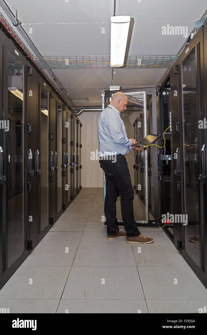 Server administrator travaillant sur ordinateur portable connecté à des serveurs à l'intérieur d'une salle de serveur Banque D'Images