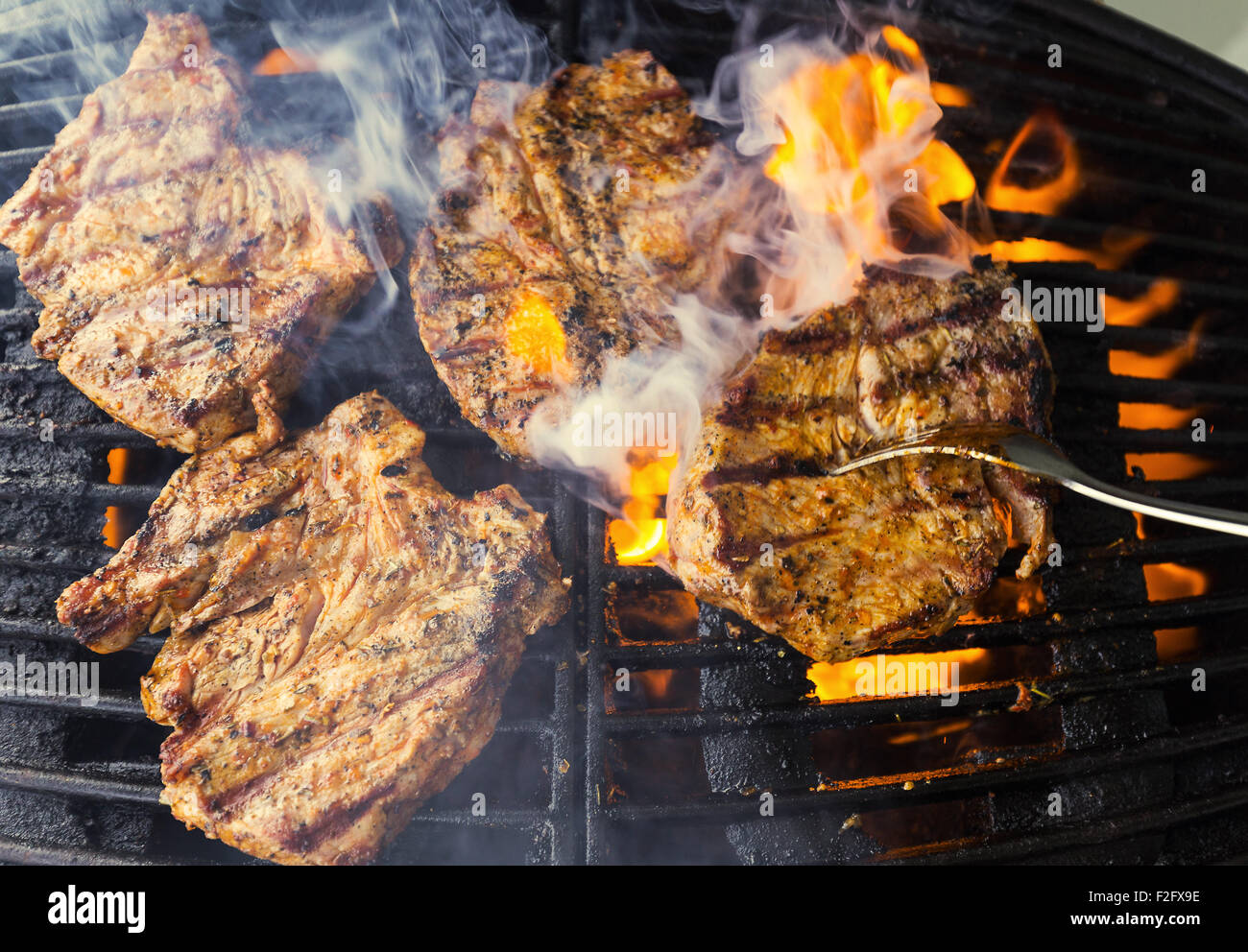 Côtelettes de porc, sauce barbecue au gaz sur l'être, des flammes léchant la viande de ci-dessous, l'homme avec un retournement de la fourche sur les côtelettes Banque D'Images