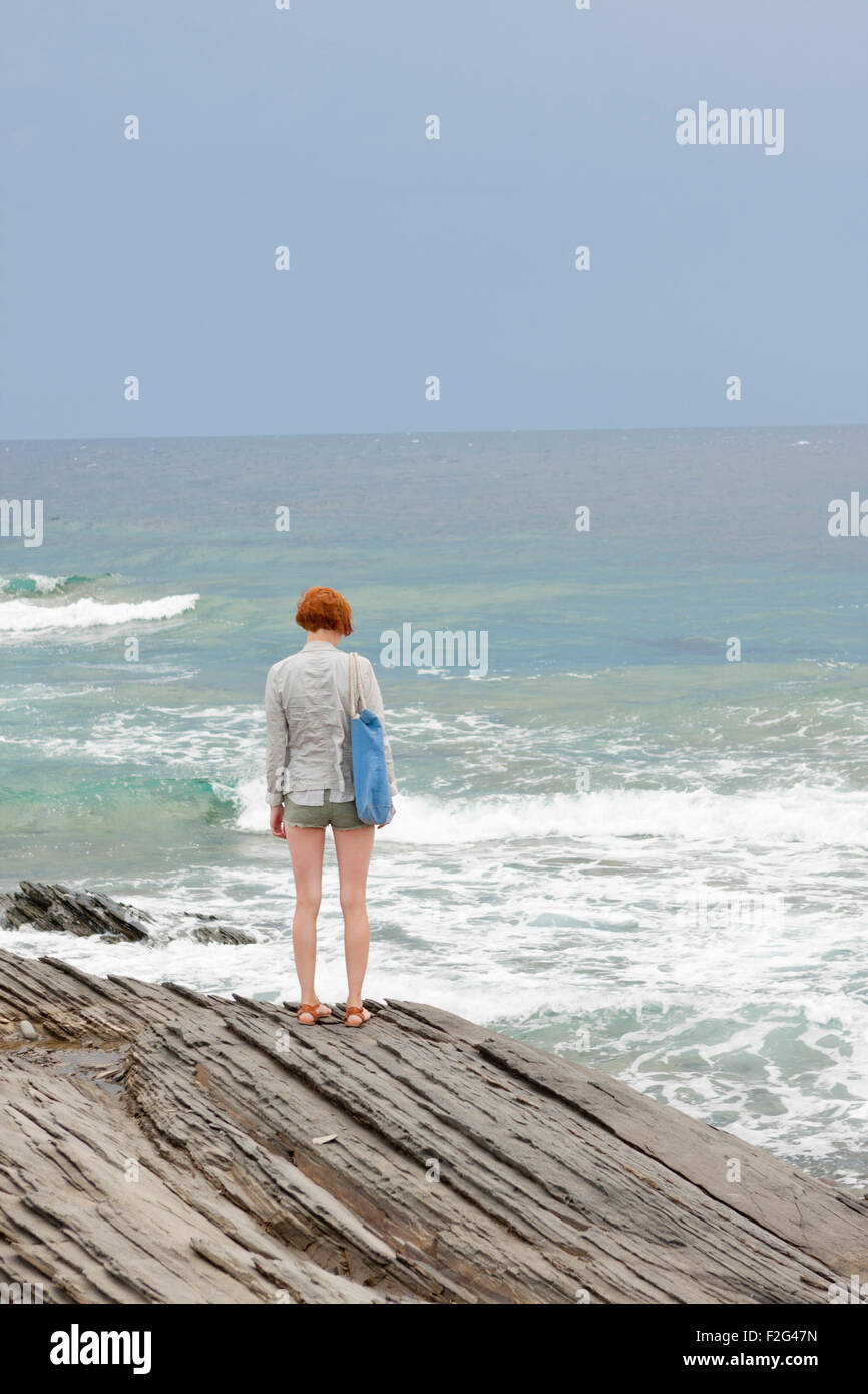 Fille aux cheveux rouges se dresse sur falaise en Minorque mer en arrière-plan Banque D'Images
